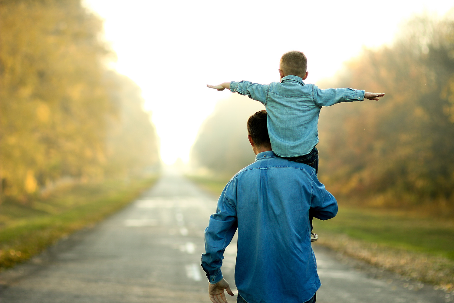 Father holding his son on his shoulders walking down a path. Need support with parenting? Alyssa Meyer offers parent coaching.