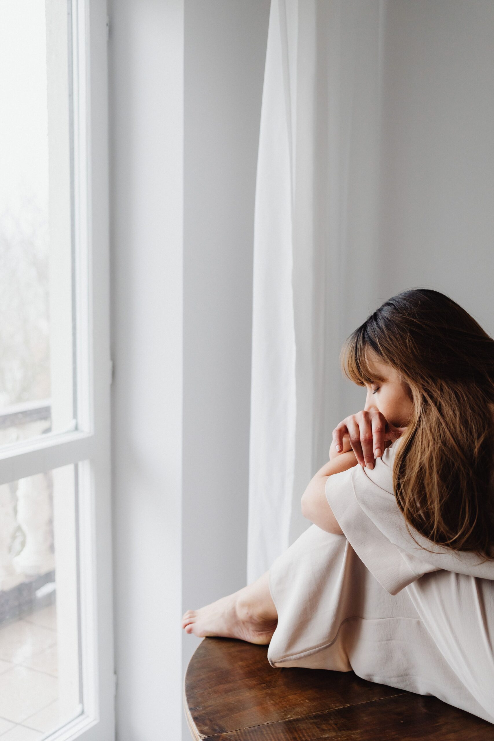 Support for Anxiety-Worry-and-Stress Adult sitting thoughtfully beside a window in a softly lit room.